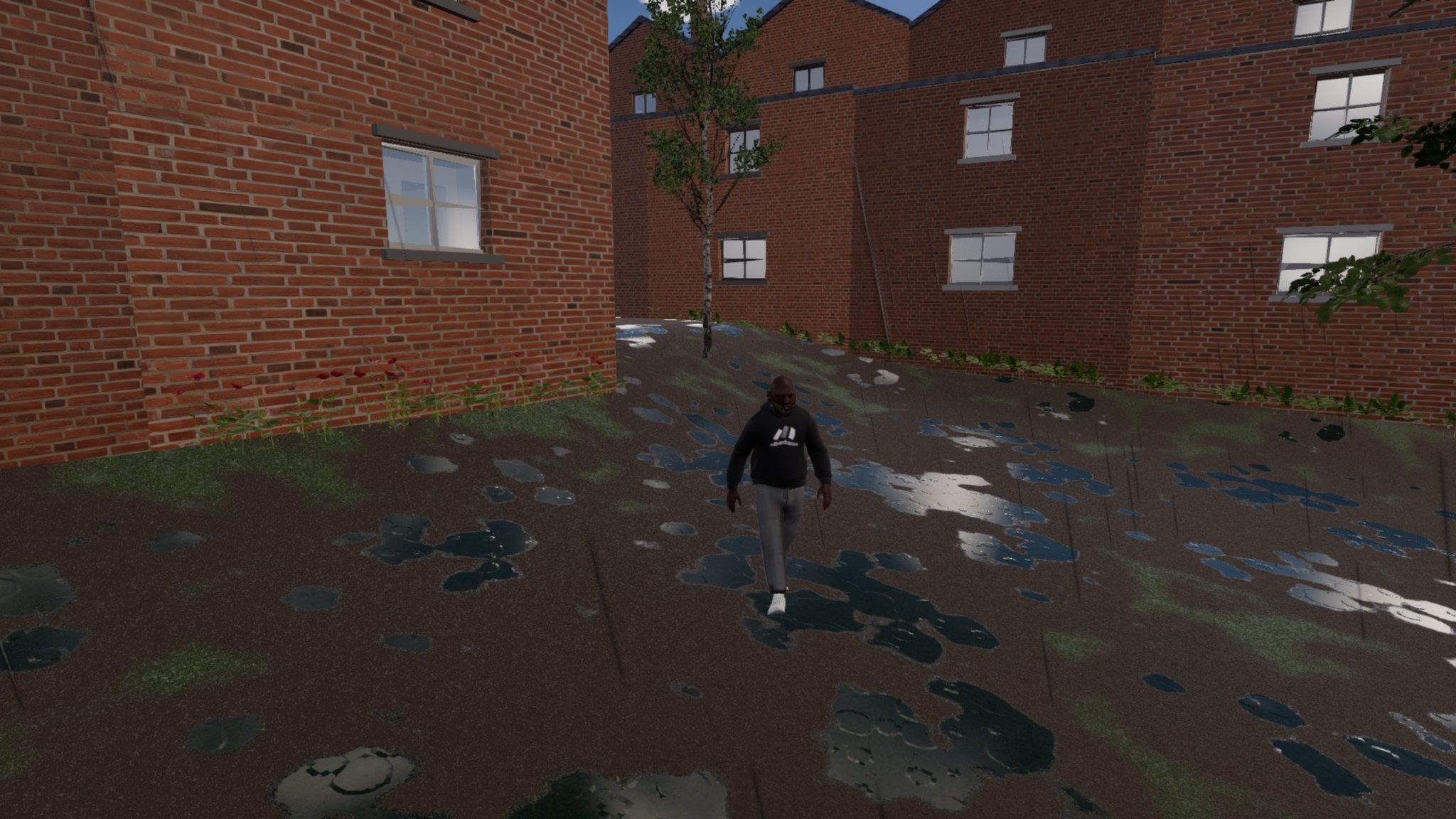 A man in a black hoodie with a small white logo, grey joggers and white trainers walks towards the camera across a wet back plot between red-brick terraces, puddles reflecting the sky.
