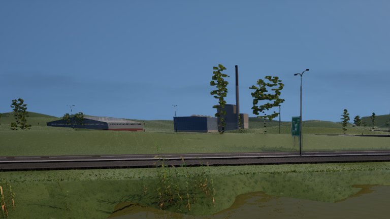 Across a river and a ring road, a long blue industrial hall and a tall thin chimney stand in open fields under a blue sky.